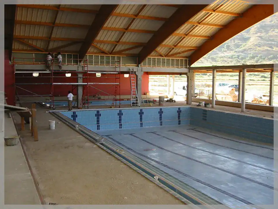 Piscina cubierta en construcción en Monzón, con estructura de madera y grandes ventanales.