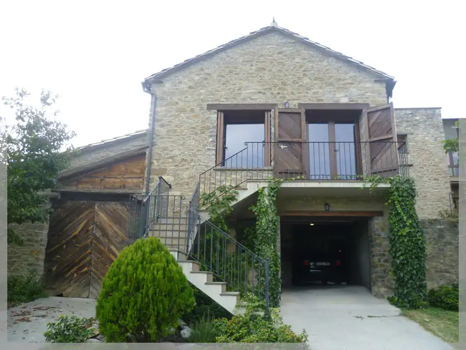 Casa unifamiliar en Labuerda con fachada de piedra y madera, con balcón y jardín, diseñada por MTArq.